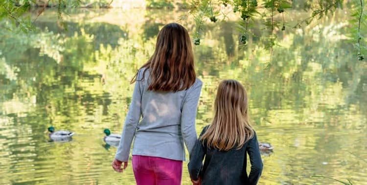 Two girls walking by a pond with ducks