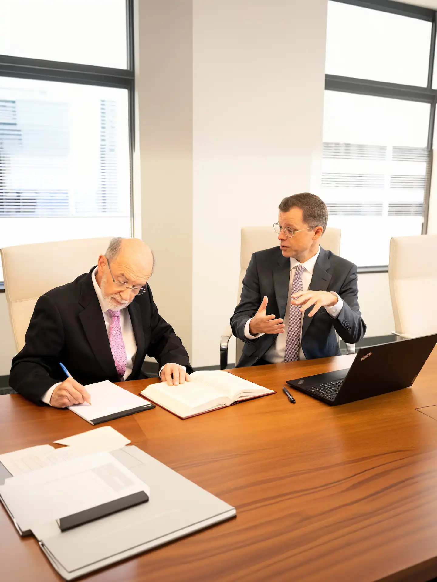 there are two men sitting at a table with papers and laptops