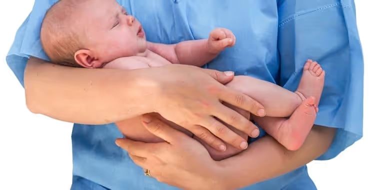 Hands in medical scrubs holding a newborn baby